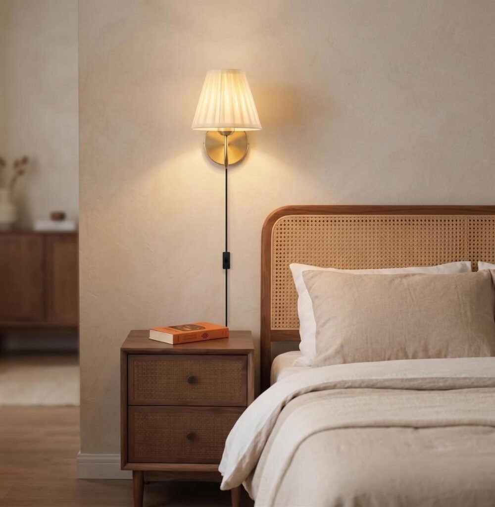 Plug-in brass wall sconce with pleated shade mounted above a clean bedside table.